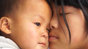 In a still from All About My Sisters, a Chinese woman holds a baby close to her face with her eyes closed. The image is a close-up of the two of them.