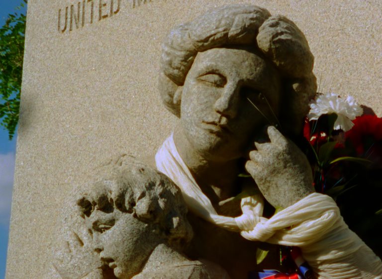 In a still from Profit Motive and the Whispering Wind, a portion of the Ludlow Monument can be seen. The sculptured monument depicts a woman holding a child tightly against her chest.