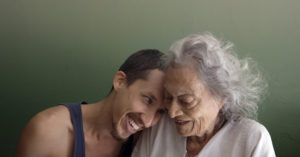 Diego leans on the shoulders of his grandmother, América. They are smiling broadly and affectionately at each other.