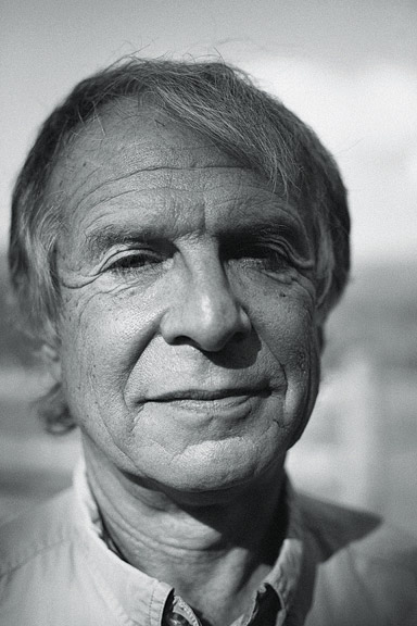 The image is a black and white portrait of filmmaker Ed Pincus. He was an older white man with white hair and his face is partially hit by shadows from light.